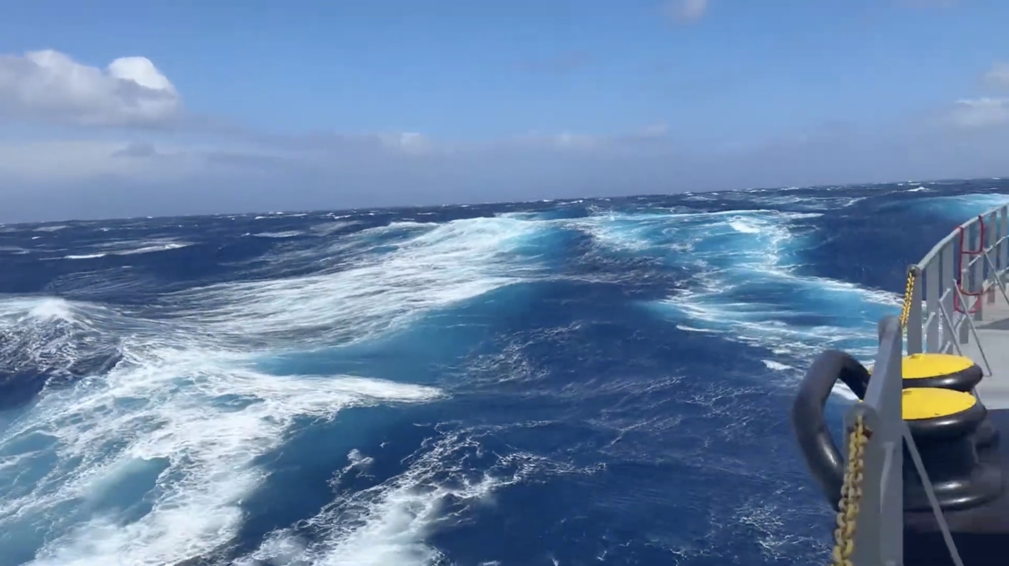 O mar visto da amurada de um navio — azul profundo, esteira turquesa, espuma branca